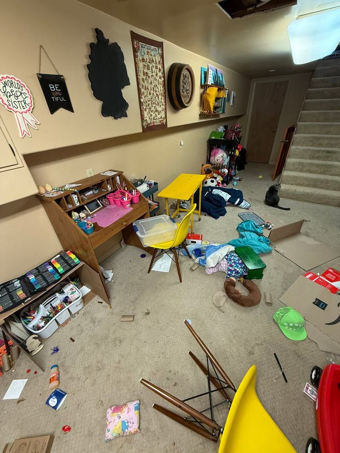 A basement corner before: toys, papers and a tipped chair over the carpet.